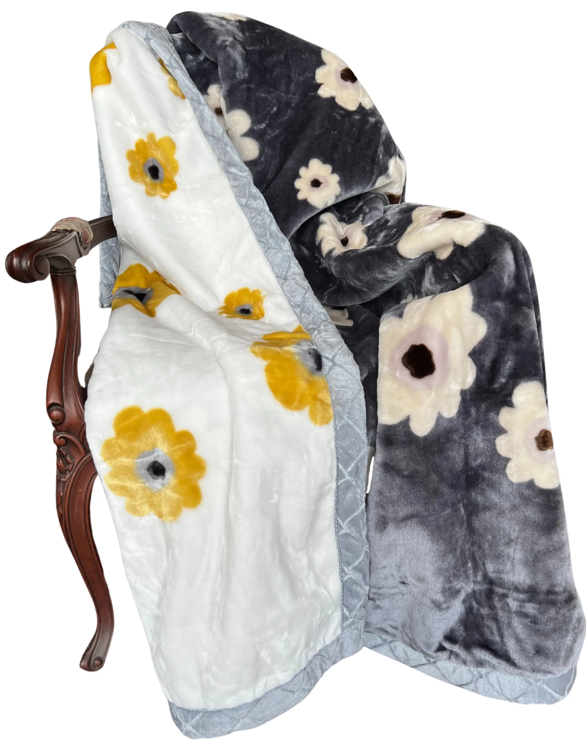 Reversible plush floral blanket on a wooden chair; gray and white sides with yellow daisies and light‑gray quilted trim.